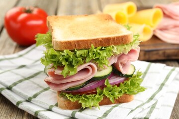 Tasty sandwich with ham and vegetables on wooden table, closeup
