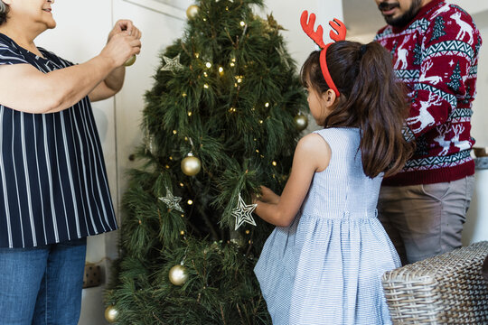 Latin Family with little girl or father and daughter with grandparents decorating christmas tree at home in mexico Latin America, hispanic people in holidays	