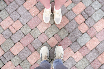 Feet in shoes on a background of paving stones, meeting, walking. Pavement and landscape paving stone background. The surface of the footpath, top view.