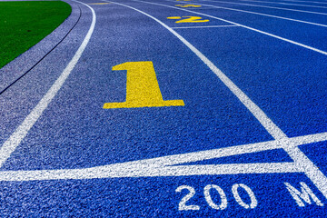 Close up photo of outdoor running track lane yellow number one, 1, on a new blue track with white lane lines.