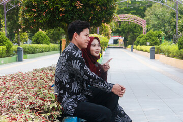 Indonesian couple in a happy moment in a park with the man wearing traditional Indonesian batik and the woman wearing an academic dress and decorated with a red hijab