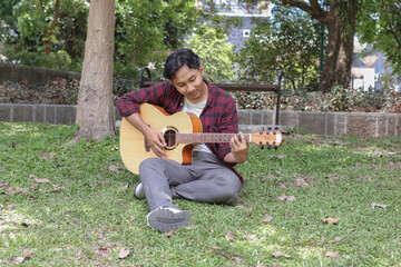 Outdoor shot of attractive Asian man playing guitar at city park in the morning