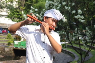 Portrait of Balinese Asian man playing traditional bamboo flute in outdoor park