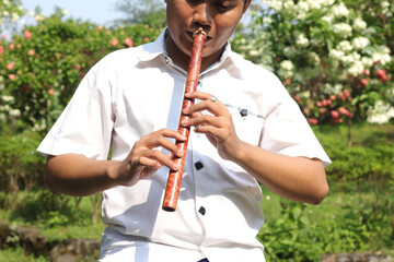 Portrait of Asian man wearing balinese traditional cloth playing bamboo flute in outdoor park © Yazid Nasuha
