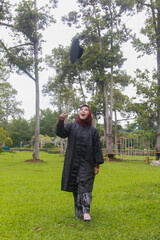 Beautiful Indonesian Muslim woman wearing maroon hijab and toga and academy dress appears elegant in a park