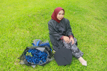 Beautiful Indonesian Muslim woman with a happy smiling expression sitting on the green grass