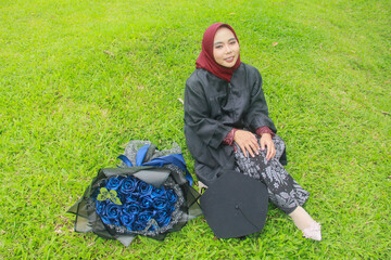 Beautiful Indonesian Muslim woman with a happy smiling expression sitting on the green grass