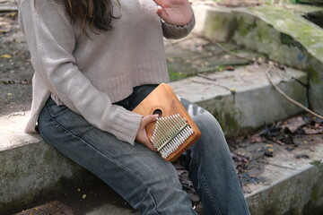 Asian woman plays a kalimba in a green park on a sunny day. The calm melodies and lush leaves...