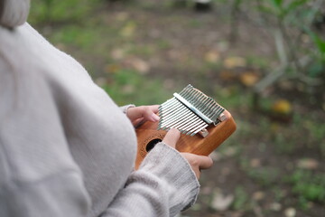 woman playing a kalimba in a vibrant park filled with green leaves on a warm summer day