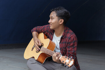Portrait of Asian man playing guitar in outdoor park