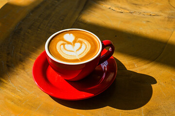 Close up view of hot cafe latte on the wooden table. red cup or mug. art. brown. dark, black, shadows. morning. relax, coffee time. cafe. coffee shop. sun shine, light. ceramic.