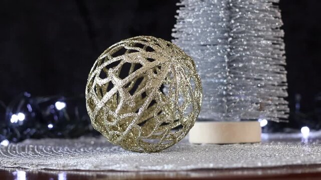 Una toma de cerca de una bola de navidad dorada y un &aacute;rbol plateado rodeados de luces blancas con un fondo desenfocado. Decoraci&oacute;n de navidad y fin de a&ntilde;o