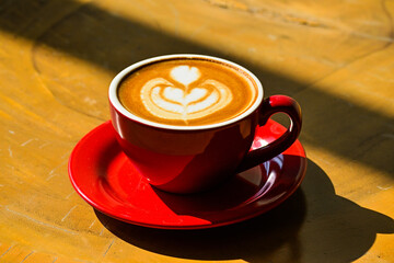 Close up view of hot cafe latte on the wooden table. red cup or mug. art. brown. dark, black, shadows. morning. relax, coffee time. cafe. coffee shop. sun shine, light. ceramic.