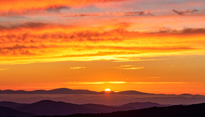 Obraz premium Sunset over the Mountain Landscape: The sun dips below the horizon, painting the sky with fiery hues of orange and red.