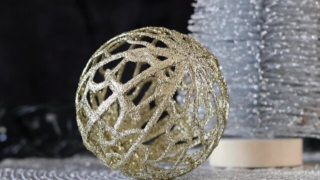 Una toma de cerca de una bola de navidad dorada y un &aacute;rbol plateado rodeados de luces blancas con un fondo desenfocado. Decoraci&oacute;n de navidad y fin de a&ntilde;o