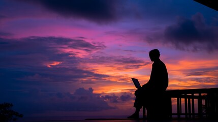 Obraz premium Silhouette of man working on laptop during vibrant purple and orange sunset