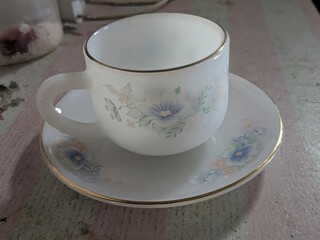 A delicate white teacup and saucer set adorned with a floral pattern and a gold rim.