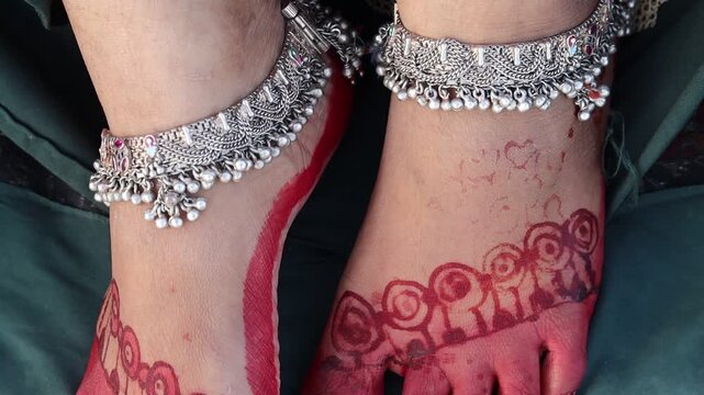 Indian woman&rsquo;s feet decorated with red alta, mehndi, silver anklets, and toe rings, dressed in traditional attire for festival or wedding celebration