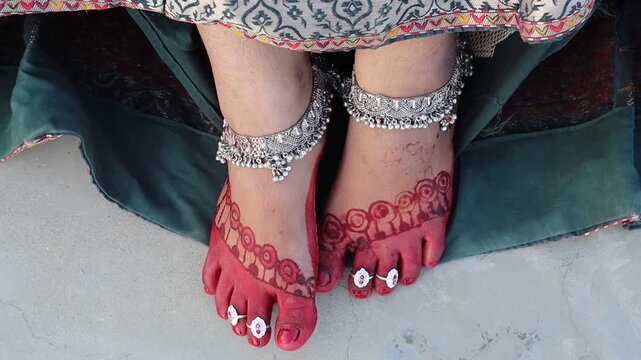 Indian woman&rsquo;s feet decorated with red alta, mehndi, silver anklets, and toe rings, dressed in traditional attire for festival or wedding celebration