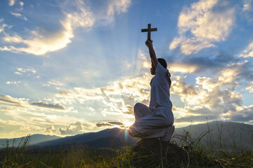 A girl holding a cross raise hands kneeling down to heaven praying to God