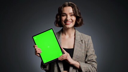 Portrait of a smiling young businesswoman holding a tablet with a green screen on a dark background. - Powered by Adobe