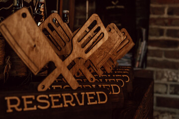 in warm restaurant atmosphere, wooden reserved signs shaped like spatulas and forks are lined up on shelf, creating unique and inviting dining experience for guests. close up.