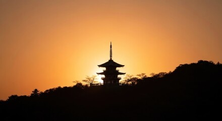 Obraz premium Silhouetted pagoda against a bright, warm sunset sky, on a forested hill