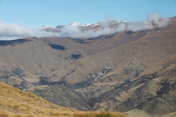 May 18, 2025: Crown Range Summit, New Zealand. Winding alpine road through rugged mountains with Queenstown and its airport visible in the stunning Wakatipu Basin. Scenic winter autumn landscape.