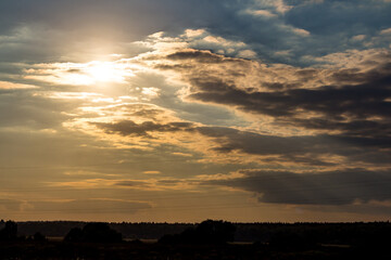 Dramatic sun breaking through heavy clouds, casting golden light over a distant silhouetted horizon