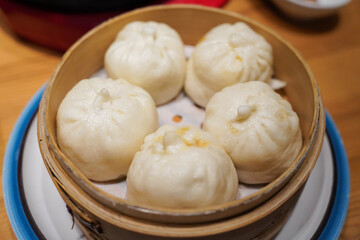 Traditional chinese baozi steam buns in a bamboo steamer basket close-up on the table.