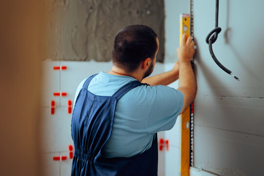 Construction Worker Using a Leveling Straightedge for Tile Installation. Skilled constructor measuring for accurate installing faience tiles 
