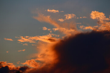 Dramatic sunset clouds with fiery orange hues contrast against a dark, ominous cloud and serene blue sky, creating a powerful natural scene