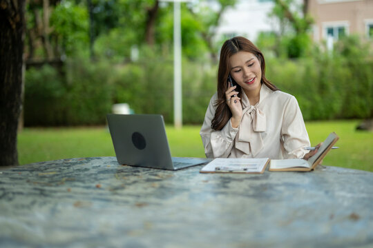 Asian woman remote working in park talking on phone