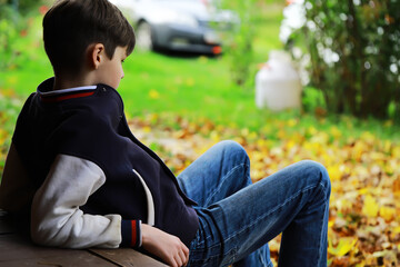 Obraz premium Boy Relaxing in Autumn Garden Wearing Casual Jacket and Blue Jeans