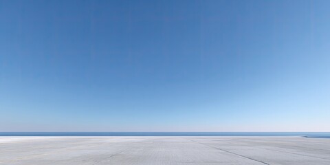 Wide, empty expanse of light gray concrete floor meets a cerulean blue sky, with a hazy horizon line of sea water