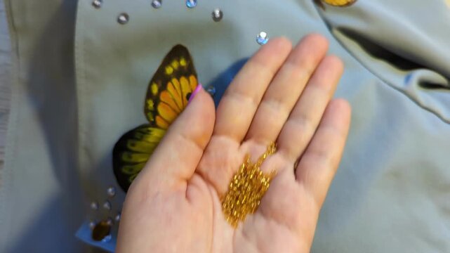 Close-up of female hand with golden glitter decorating a painted butterfly on fabric. Creative handmade art, textile embellishment, and fashion design concept. Clothing customizing.
