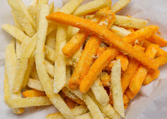A high-angle close-up shot of a mix of golden-yellow french fries, some lightly seasoned with salt and herbs, mixed with others generously coated in bright orange cheese powder.