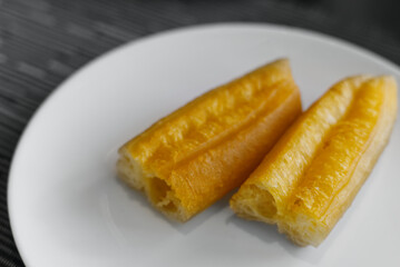 A close-up of two pieces of Youtiao (Chinese oil stick/doughnut) on a bright white plate. 