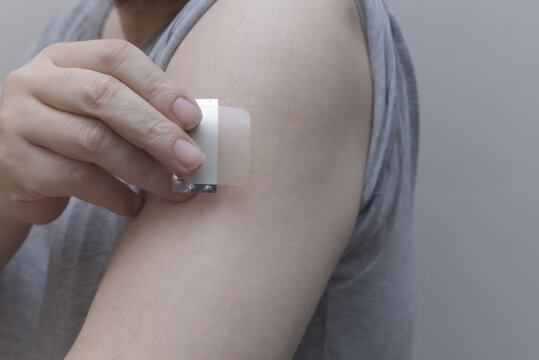 A close-up of a hand applying a nicotine patch to the upper arm. Represents Nicotine Replacement Therapy (NRT) and the user's commitment to quit smoking and pursue better health