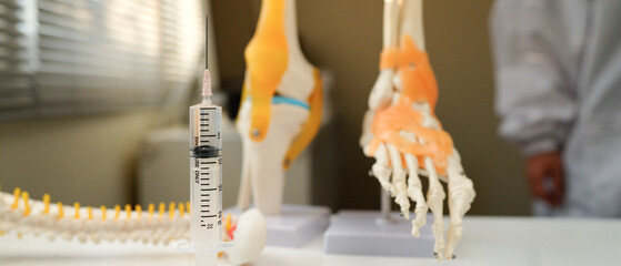 A syringe is on a table next to a model of a knee. The syringe is filled with a liquid and is ready to be used. Concept of preparation and anticipation for a medical procedure