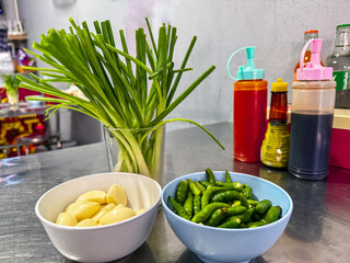 Fresh scallions, peeled garlic, fresh chilies, and seasonings are laid out on the Thai dining table.