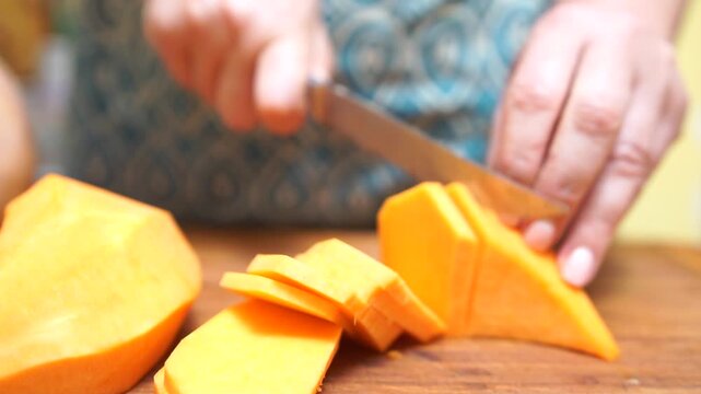 Slicing vegetables pumpkin. Female hands cut carrot on a wooden cutting board. Cooking in the kitchen. Food preparation. Close-up.