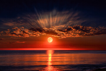 Radiant full moon rising over calm ocean waters with dramatic clouds illuminated by warm orange and red hues during tranquil evening twilight sky