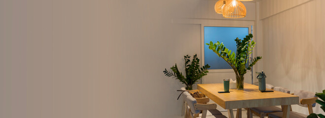 Modern wooden dining table with green plants and warm hanging lights in cozy minimalist home interior