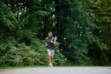 Man jogging along a tree-lined park road, focused on fitness and wellness with determined stride...