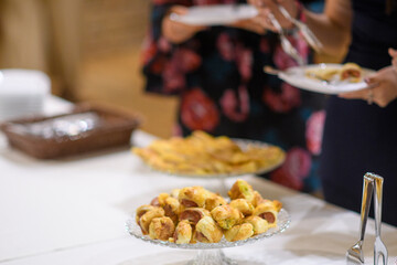 Delicious Sausage Wrapped in Flaky Pastry served at a catered event with other appetizers in the background and guests in attendance
