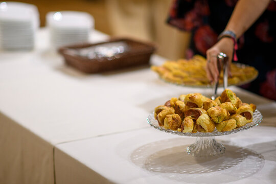 Close up of golden brown pigs in a blanket appetizers being served from a clear glass cake stand at an event or party with shallow depth of field