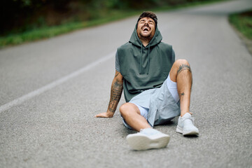 Bearded runner sitting on urban pavement, laughing and catching breath after a joyful outdoor workout — relaxed, energetic, carefree