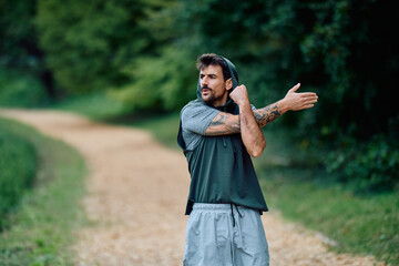 Man in athletic wear warming up, stretching his arm in a nature park. Focusing on fitness,...