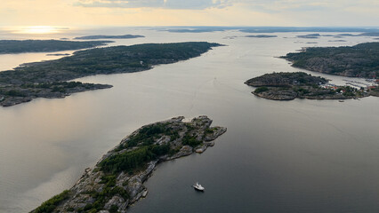 Drone Aerial of Island Channel Near Str&ouml;mstad, Sweden with Rocky Shores, Greenery, and a White Boat Floating on Calm Water at Sunset